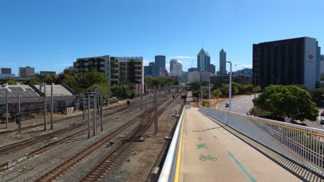 Cyclepath-down-ramp-running-alongside-rail-track-at-Claisebrook-station-Perth,-with-city-in-background