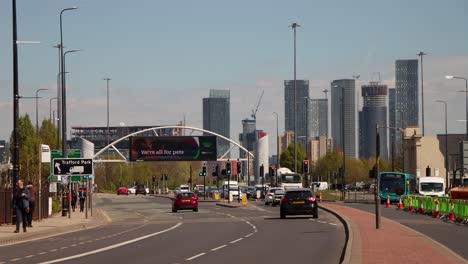 Cars-wait-at-traffic-light-as-public-bus-leaves-Manchester-and-Castlefield-skyscraper-skyline-at-midday