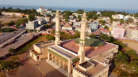 Panorama-Aéreo-Deslizante-De-La-Mezquita-Del-Rey-Fahad-De-Banjul-Con-El-Arco-22-En-El-Fondo-Y-Un-Hermoso-Paisaje-Urbano-Del-Centro-Africano