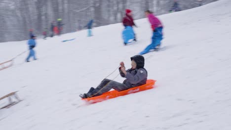 A-Boy-Sliding-Down-a-Snowy-Slope-on-a-Sled-at-Woluwe-Park,-Brussels,-Belgium---Tracking-Shot