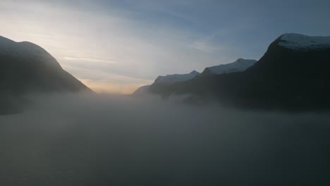 Misty-dawn-breaks-over-Oppstrynsvatnet-lake-in-Norway,-mountains-silhouetted