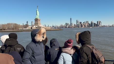 Menschen-Fahren-Mit-Der-Fähre-An-Der-Freiheitsstatue-Vorbei,-In-Der-Ferne-Ist-Die-Innenstadt-Von-Manhattan