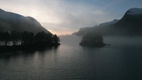 Misty-dawn-over-Oppstrynsvatnet-in-Norway-with-serene-waters-and-mountain-backdrop,-aerial-view