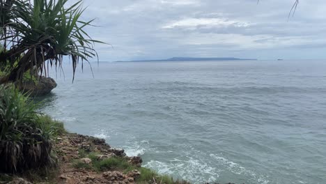 Toma-Fija-De-Un-Paisaje-Oceánico-Mientras-Las-Olas-Golpean,-El-Agua-Salpica-En-La-Orilla-Del-Mar,-La-Isla-En-La-Distancia