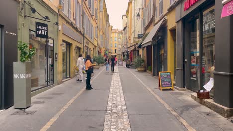 People-walk-through-colorful-street-in-Aix-en-Provence,-France,-daytime,-urban-vibe