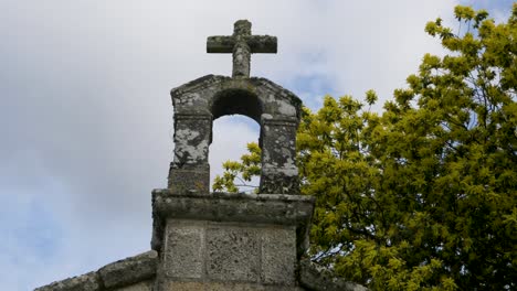 Low-angle-looking-up-at-carved-stone-cross-and-moss-lichens-and-yellow-green-blossoms-at-Chapel-of-San-Vitoiro
