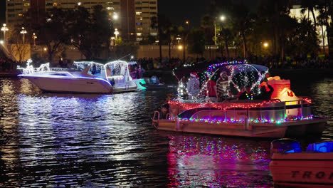 Botes-Pontones-Y-Lanchas-Rápidas-Envueltas-En-Vibrantes-Luces-Navideñas-De-Color-Rojo,-Azul-Y-Violeta-Desfilan-Por-El-Agua