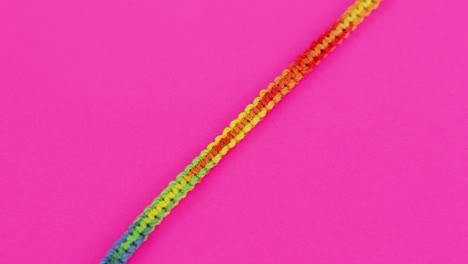 Close-up-shot-of-colorful-and-vibrant-threaded-macrame-bracelet-with-rainbow-color-pattern,-resting-on-neon-pink-background