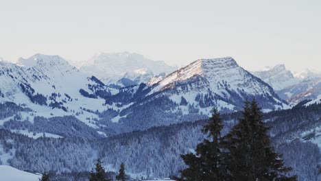 Toma-Aérea-Del-Amanecer-Que-Muestra-La-Silueta-De-Las-Montañas-Cubiertas-De-Nieve.