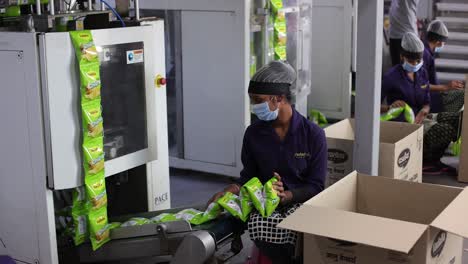 pov-shot-packets-of-chips-coming-out-of-machine-men-packing-in-chips-packing-in-boxes