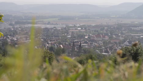 Hazy-view-of-a-European-town-with-spires,-nestled-in-a-valley,-from-a-blurred-foreground-of-grass