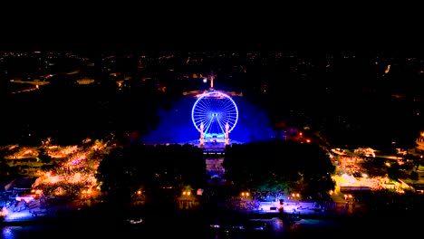 Illuminated-Ferris-wheel-at-night-during-Wine-Fair-and-crowd-nearby-in-Bordeaux-France,-Aerial-tilt-up-shot
