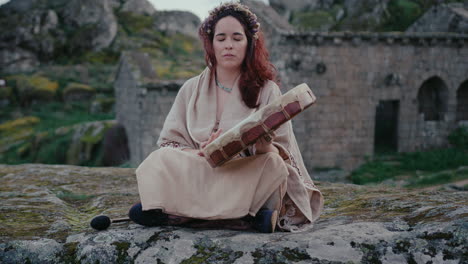 spiritual-woman-playing-a-shamanic-drum-in-a-beautiful-medieval-village-long-shot