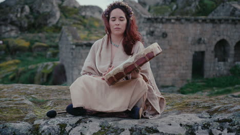 Mujer-Espiritual-Tocando-Un-Tambor-Chamánico-En-Un-Hermoso-Pueblo-Medieval.