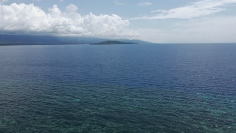 A-tranquil-blue-sea-with-a-lush-green-island-under-a-clear-sky,-aerial-view