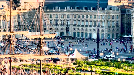 People-gathered-in-Place-de-la-Bourse-plaza-square-during-Wine-Fair-with-a-sailing-ship,-Aerial-dolly-right-shot