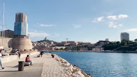People-relax-by-water-at-old-port-on-sunny-day-in-Marseille,-France