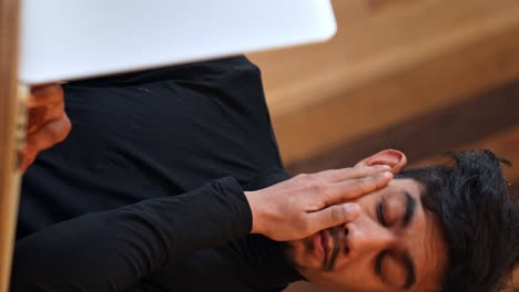 Tired-and-stressed-Sri-Lankan-man-working-in-front-of-his-laptop,-vertical-view