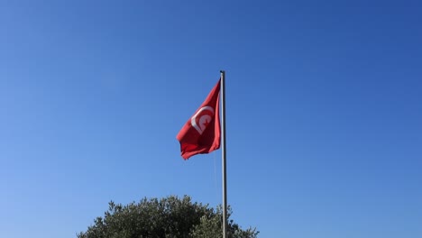 Rote-Tunesische-Flagge-Weht-Im-Klaren-Blauen-Himmel,-Symbol-Des-Nationalstolzes