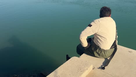 Capturando-A-Un-Pescador-Sentado-En-La-Plataforma-A-La-Orilla-Del-Agua,-Observando-Y-Descansando-Pacíficamente,-Encarnando-La-Esencia-De-Un-Pintoresco-Pueblo-De-Pescadores.