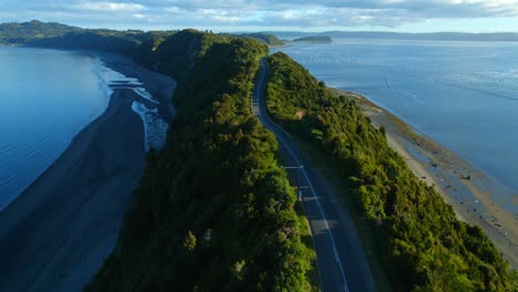 Aerial-drone-fly-above-asphalted-avenue-through-green-island-hills-at-Patagonian-sea,-Chiloé,-Chile,-travel-destination,-Lemuy-Island-connection-with-Detif