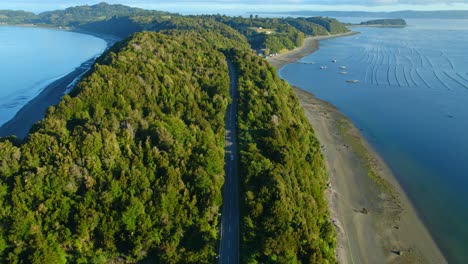 Aerial-shot-of-a-car-driving-along-a-narrow-channel-on-Lemuy-Island,-Chiloe,-lush-scenery