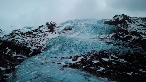 Vista-Aérea-De-Drones-De-Personas-Caminando-En-El-Campo-De-Un-Glaciar-Azul-En-Islandia,-Tierra-De-Fuego-Y-Hielo