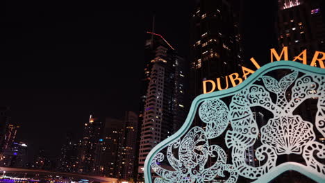 Dubai-Marina-Sign-at-Night-in-Front-of-Skyscrapers,-Panorama