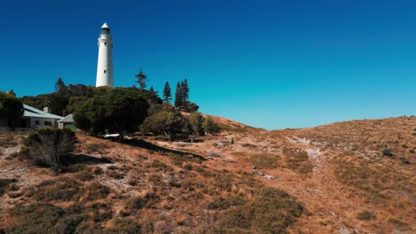 drone-shot-over-wadjemup-lighthouse-on-Rottnest-Island-on-a-sunny-day-revealing-the-seashore-behind