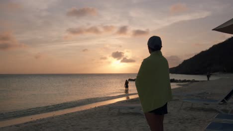 Woman-stands-on-sand-beach-as-sun-sets-over-Caribbean-Sea-at-Curaçao