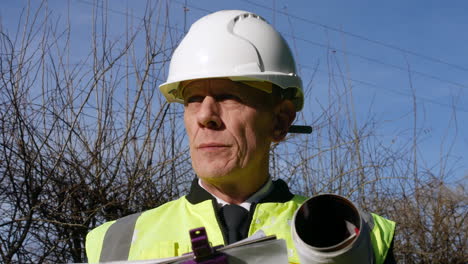 Close-up-portrait-of-an-architect-building-inspector-inspecting-a-construction-site-with-a-clip-board-and-architectural-plans