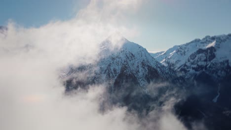 Video-Einer-Drohne,-Die-Durch-Die-Wolken-Auf-Eine-Schneebedeckte-Bergkette-Zufliegt