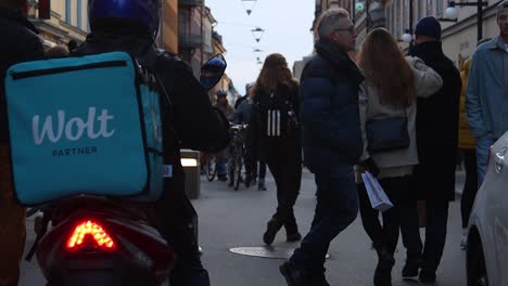 Wolt-food-delivery-scooter-on-pedestrian-street-in-Stockholm,-slomo