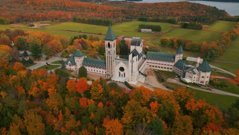 aerial-shot-around-saint-benoit-du-lac-abbey-at-fall-with-colorful-trees-near-magog-on-and-memphremagog-lake-in-quebec-region,-autumn-season,-canada