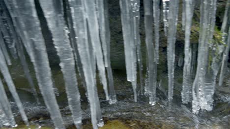 Panning-shot-of-flowing-stream-under-icicles-in-nature-of-Switzerland