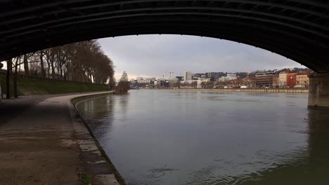 Iron-Bridge's-Vista:-A-Glimpse-Beneath,-Lyon's-Riverside-Promenade-Adorned-in-Winter's-Veil,-Inviting-Tranquility