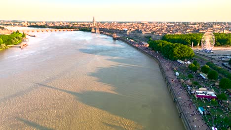 Garonne-River-and-Wine-Fair-with-Ferris-wheel-full-of-crowds-in-Bordeaux-France,-Aerial-pan-right-and-left-shot