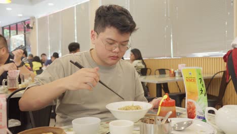 Asian-man-with-glasses-enjoying-a-bowl-of-noodles-in-a-restaurant