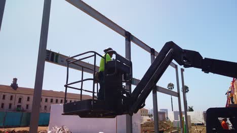 Gimbal-close-up-shot-of-a-construction-worker-lowering-in-a-cherry-picker-lift-crane-at-a-modular-building-site-in-West-Los-Angeles,-California