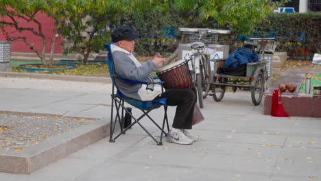 An-elderly-Chinese-man-plays-an-African-drum-in-the-park-in-Beijing