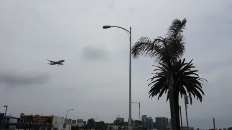 Airplane-Landing-on-San-Diego-International-Airport,-Flying-Above-Buildings-and-Streets-Under-CLoudy-Sky,-Low-Angle-View