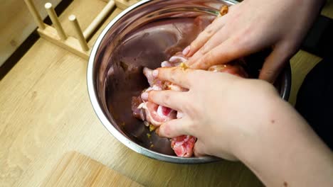 Closeup-shot-of-woman-hands-mixing-raw-chicken-pieces-with-spices-in-metal-bowl-over-on-wooden-countertop-in-the-kitchen