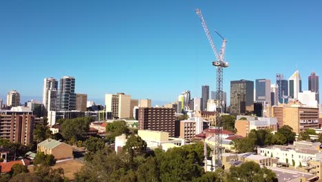 Toma-Aérea-De-Retroceso-De-Una-Grúa-Torre-Moviéndose-En-Un-Sitio-De-Construcción-Con-Una-Bandada-De-Pájaros-Volando-Sobre-Las-Copas-De-Los-árboles