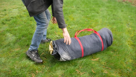 A-man-taking-a-tent-out-of-a-bag,-unpacking-it-and-laying-it-on-the-grass