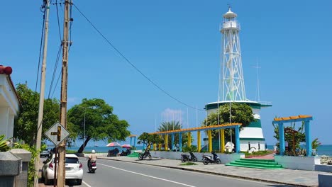Iconic-landmark-of-Farol-Lighthouse-overlooking-ocean-with-passing-traffic-along-waterfront-road-in-capital-city-of-East-Timor,-Southeast-Asia