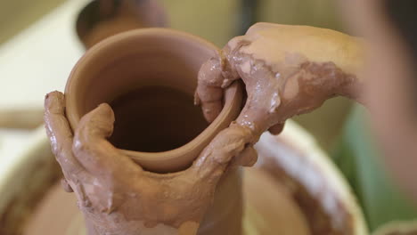 Over-shoulder-view-of-potter-working-wet-clay-rotating-on-workshop-pottery-wheel