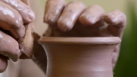 Skilled-craftsman-smoothing-raw-clay-vessel-with-wet-sponge-on-workshop-pottery-wheel