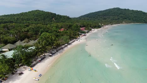 Drone-aerial-view-in-Vietnam-flying-over-Phu-Quoc-island-Sao-beach,-white-sand,-crystal-clear-blue-turquoise-water,-green-palm-trees-forest-and-people-walking-on-a-sunny-day
