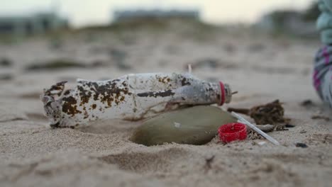 Primer-Plano-De-Un-Bebé-Recogiendo-Una-Tapa-De-Botella-De-Plástico-En-La-Playa