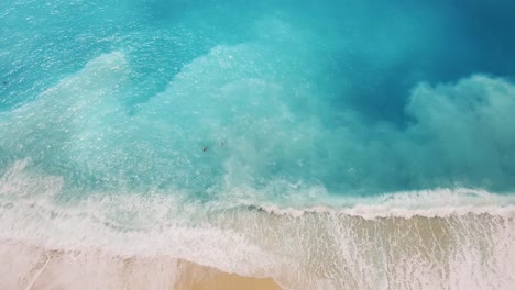 Overhead-drone-shot-of-some-beachgoers-swimming-and-playing-with-the-waves-at-the-beachfront-of-Myrtos,-located-in-the-island-of-Kefalonia-in-Greece